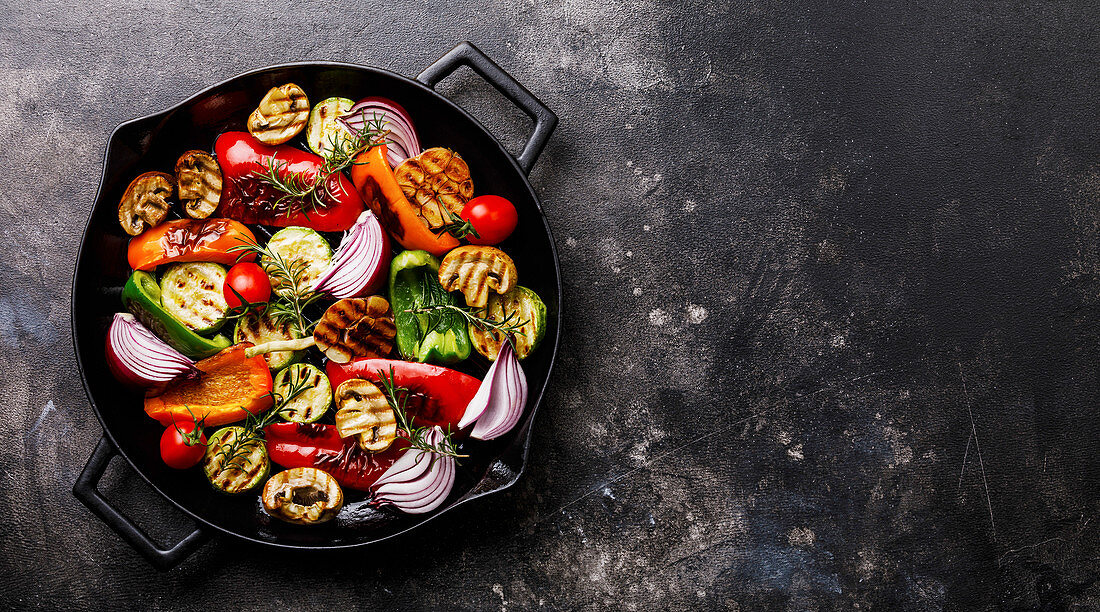 Grilled assorted vegetables in cast iron pan on dark background copy space