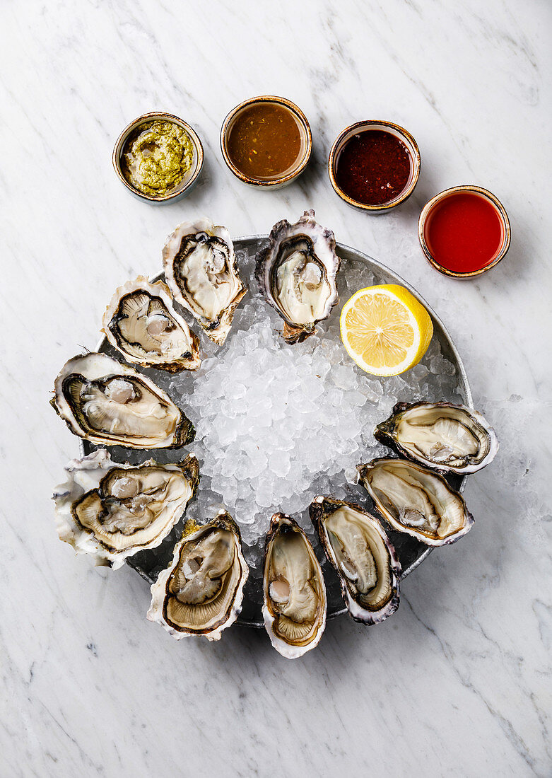 Open Oysters with lemon and sauce on white marble background