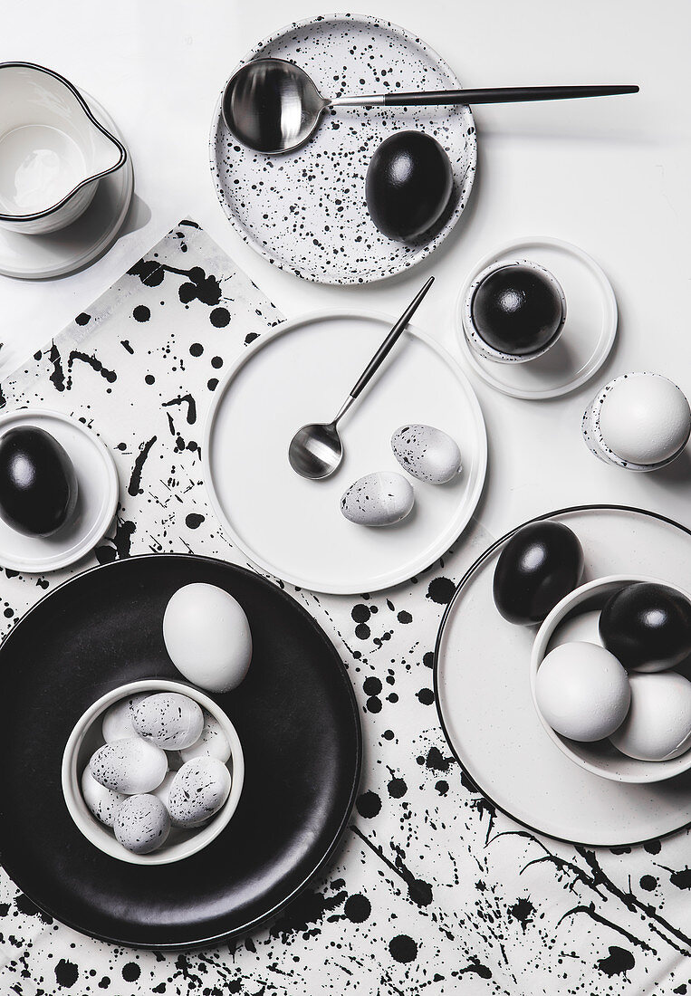 Schwarze, weiße und gesprenkelte Eier auf Tisch mit schwarz-weißem Geschirr