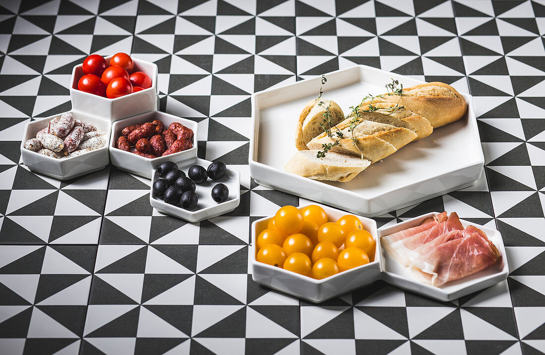 A white baguette with various antipasti on a patterned surface