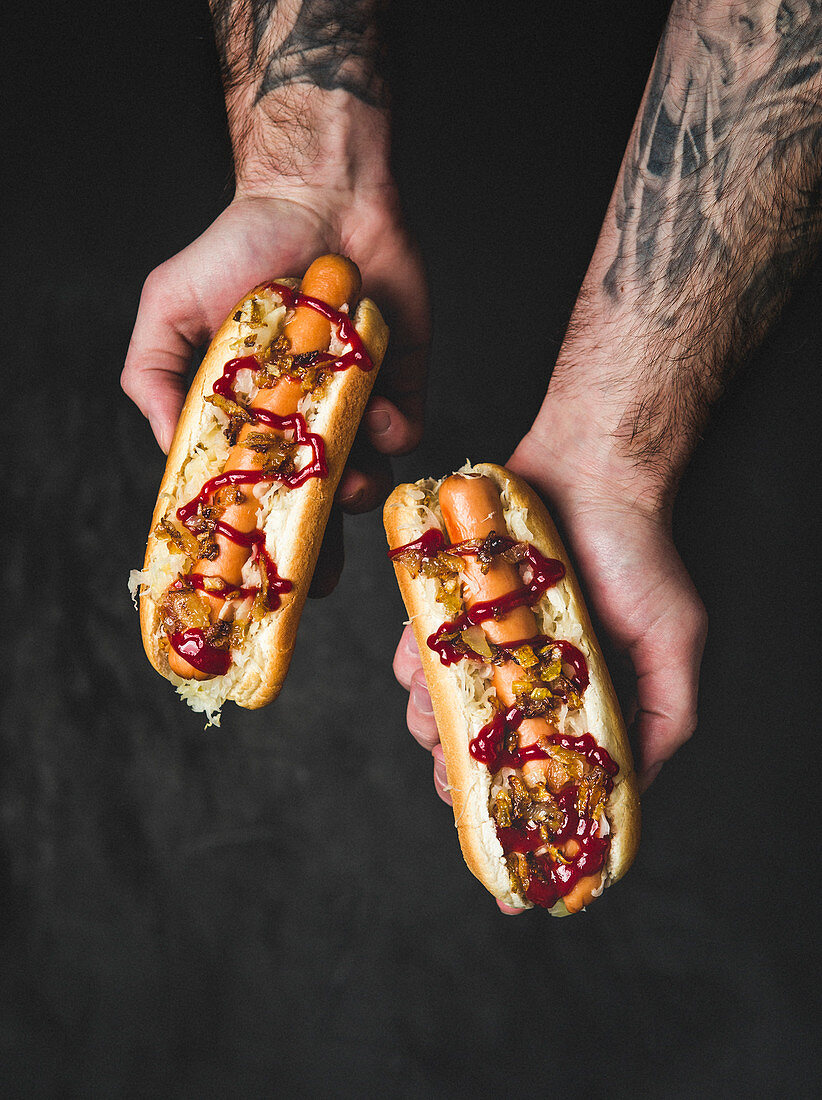 Männerhände halten zwei Hot Dogs mit Zwiebeln und Ketchup