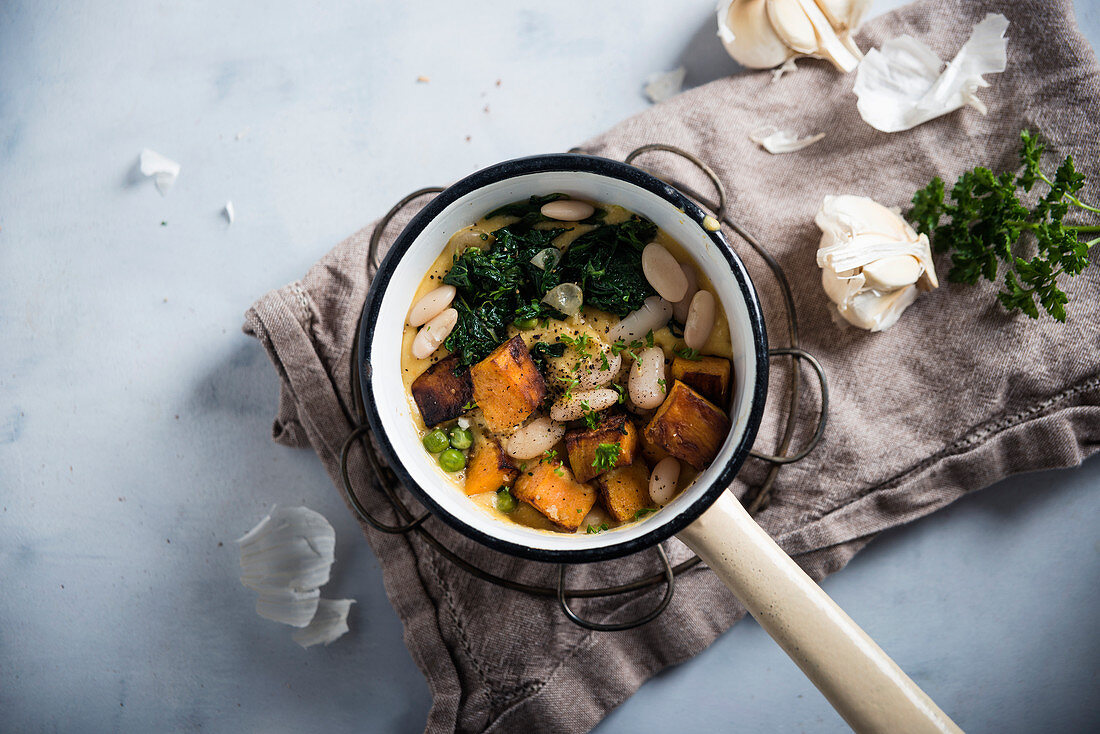 Vegan stew with roasted sweet potatoes, white beans, peas and spinach