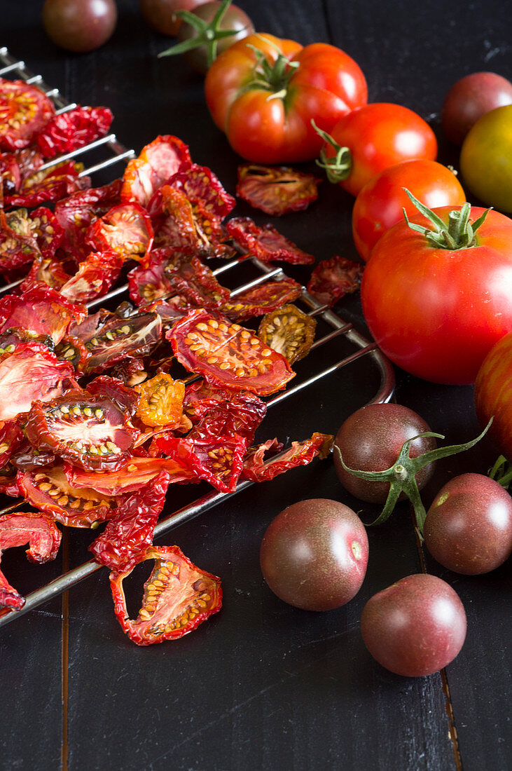 Getrocknete Tomaten auf einem Rost ausgebreitet, daneben frische, bunte Tomaten