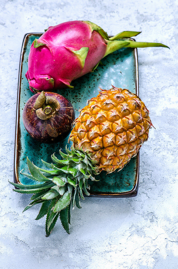 Drachenfrucht, Mangoste und Ananas auf blauem Keramikteller