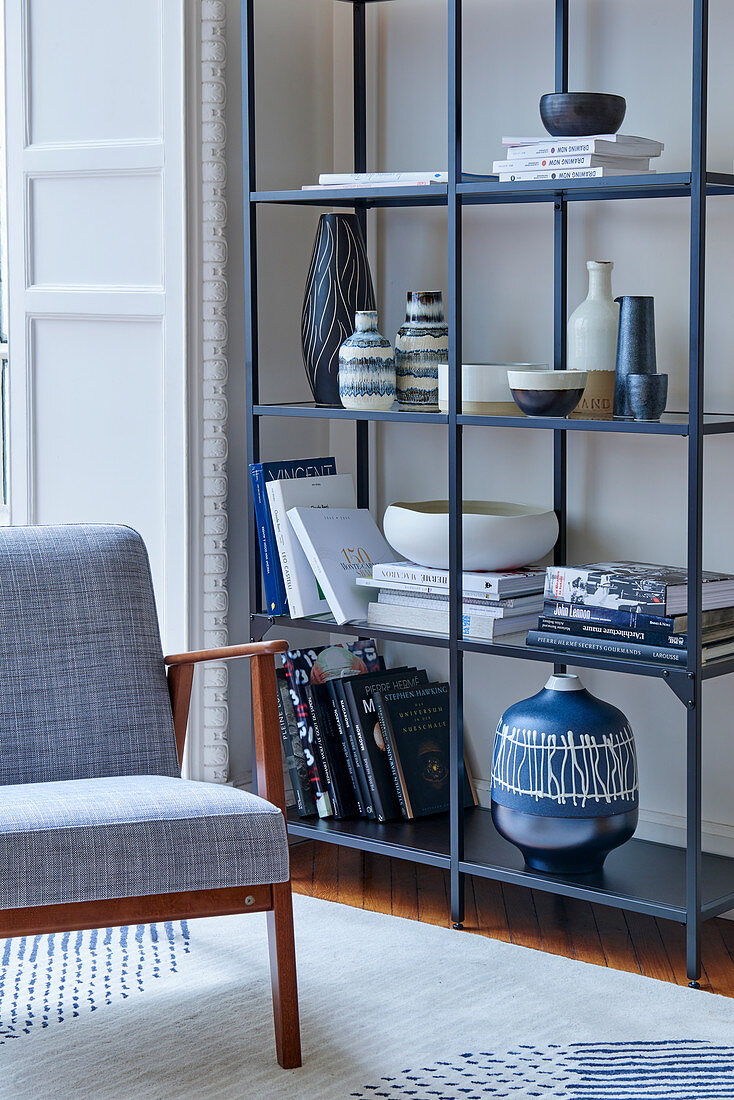 Chair with grey cover next to books and various ceramic containers on open metal shelves