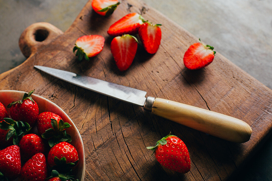 Frische Erdbeeren in Schälchen und halbiert mit Messer auf Holzbrett