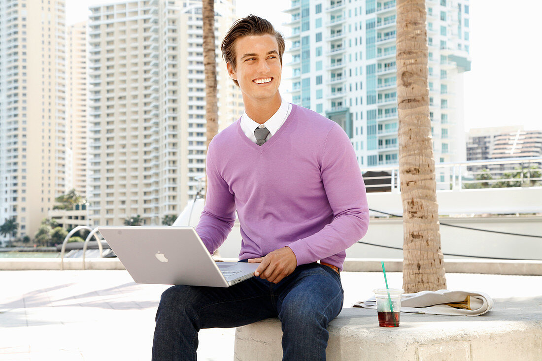 A young business man with a laptop on the street with office buildings in the background