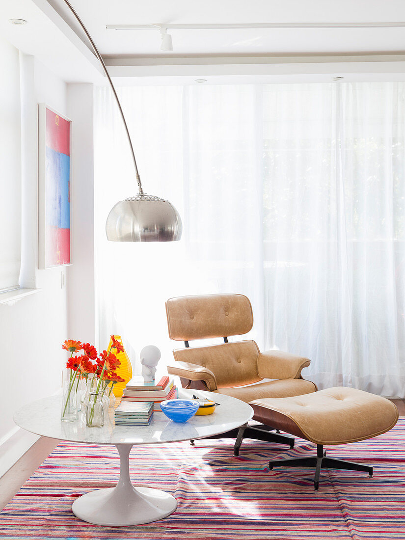 Runder, weißer Tisch und klassiker Lounge Chair mit hellem Lederbezug auf gestreiftem Teppich
