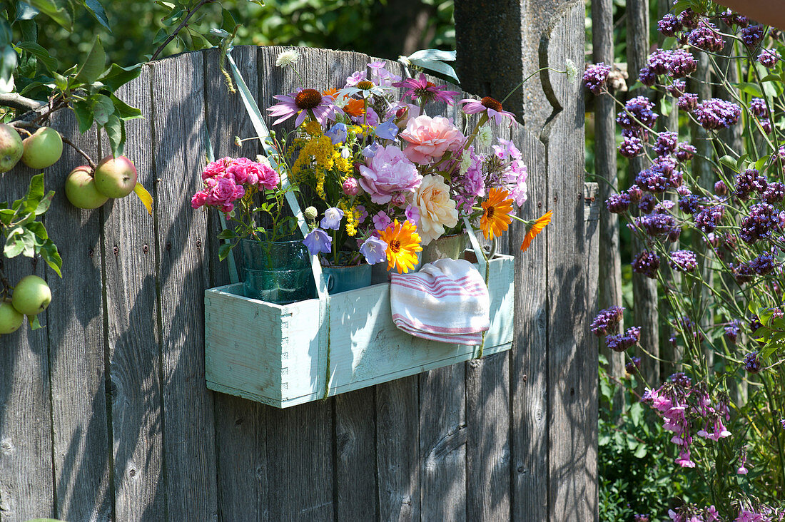 Wooden box with bouquets of roses and shrubs hung on the garden gate