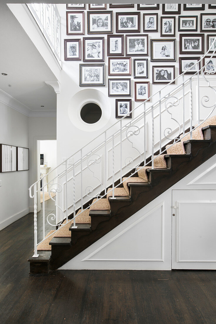 Treppenaufgang mit gerahmten, schwarz-weißen Familienfotos an weißer Wand