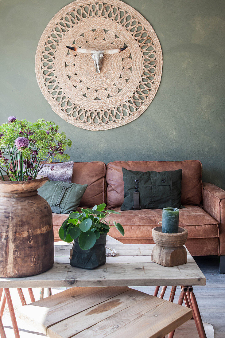 Blick über Couchtisch auf braunes Ledersofa und Wandteppich mit Tierschädel im Wohnzimmer mit grüner Wand