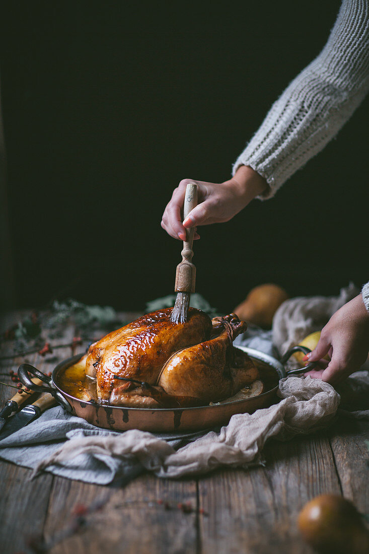 A golden roast chicken with an apple and pear glaze in a copper roasting pan on a rustic wood tabletop