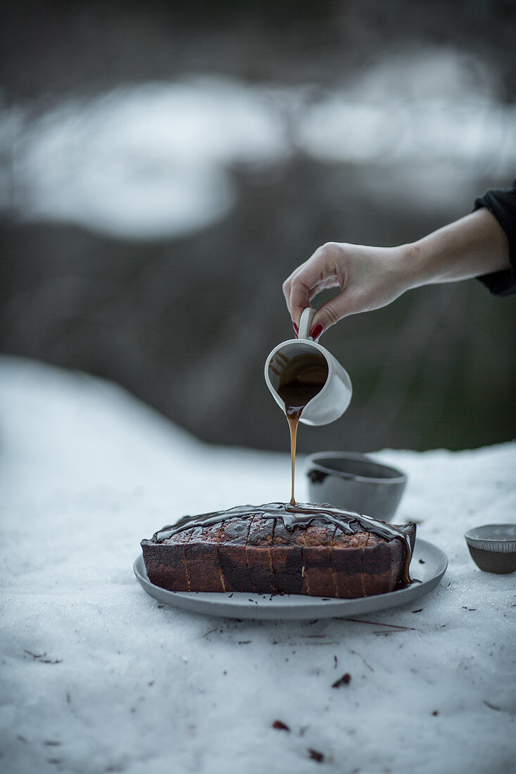 A marble loaf cake outside in the snow with a chocolate glaze drizzled on it