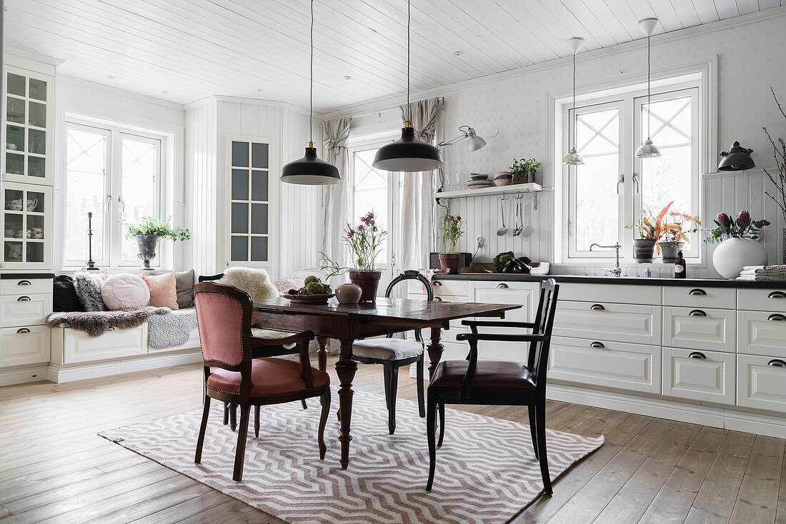 Antique dining table and chairs with window seat in background in white kitchen-dining room