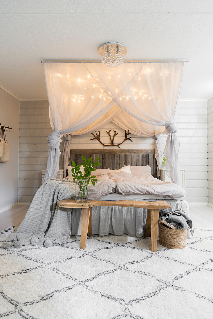 Doppelbett mit beleuchtetem Betthimmel und Holzbank in hellem Schlafzimmer