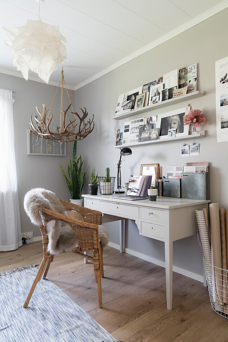 Weißer Schreibtisch, Korbstuhl und Regale an hellgrauer Wand