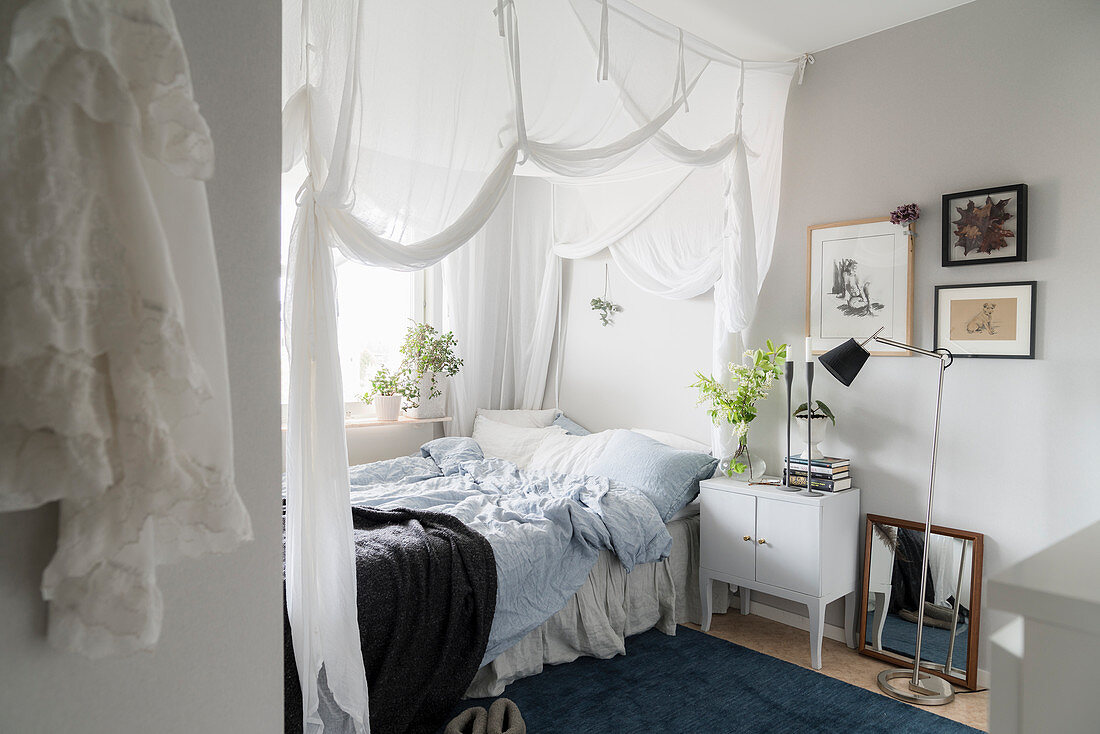 Bed with white curtains and bedside cabinet in cosy bedroom