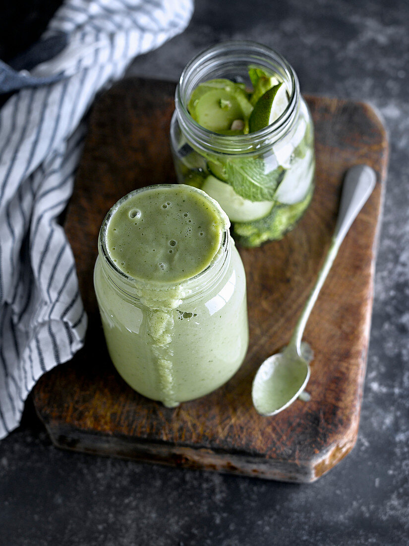 Ein Glas mit Smoothie-Zutaten und ein fertig gemixter grüner Smoothie