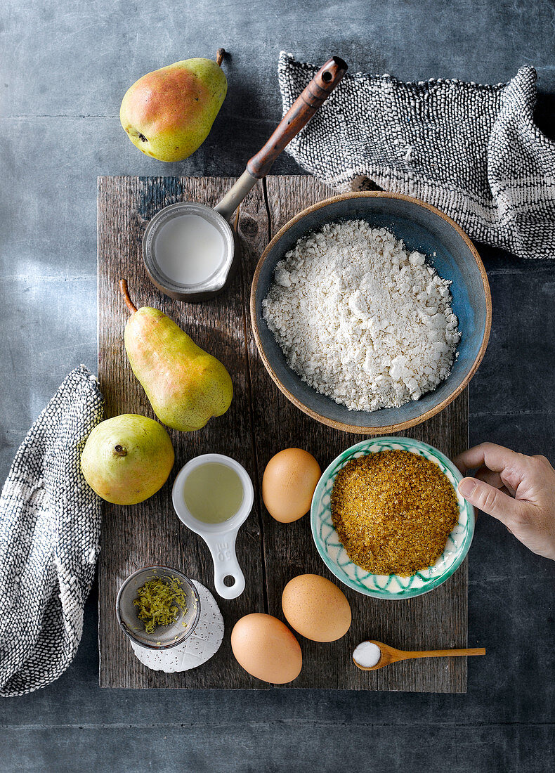 Top view of ingredients and products for preparing sweet pear cake arranged on wooden board