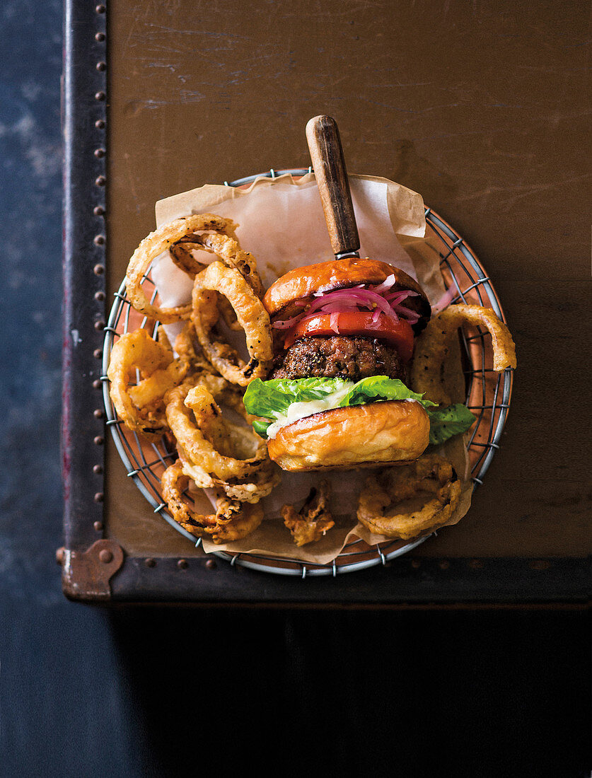 Cheeseburger serviert mit frittierten Zwiebelringen in Drahtkörbchen