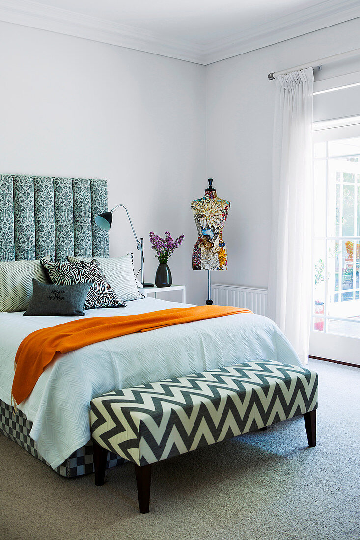 Double bed with high bed headboard and clothes bench, in the background a manikin in the bedroom