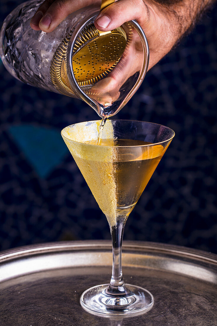 A martini being poured from a cocktail shaker into a glass