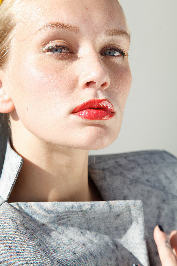 Junge blonde Frau mit rot geschminkten Lippen in grauem Oberteil