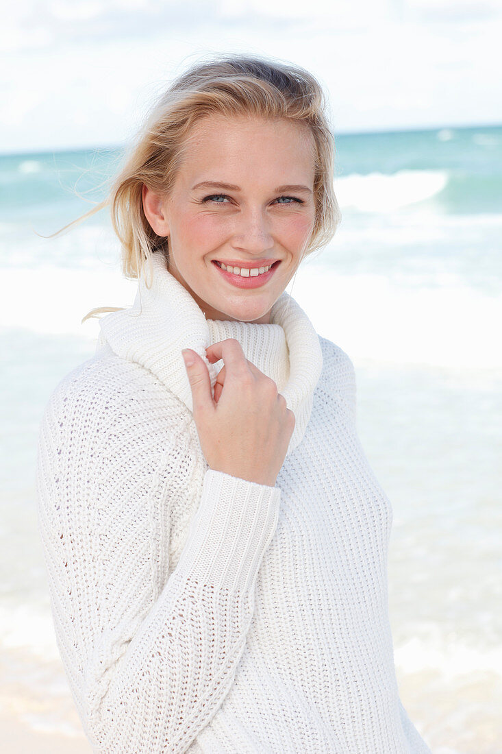 A young blonde woman by the sea wearing a white jumper