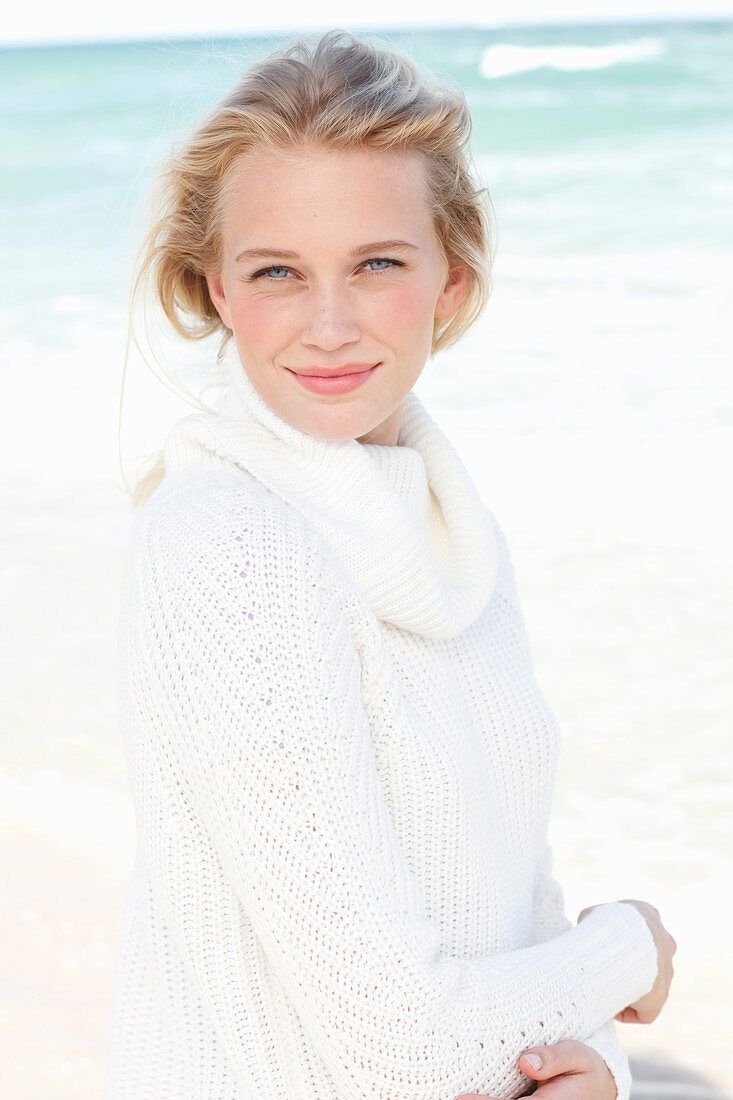 A young blonde woman by the sea wearing a white jumper