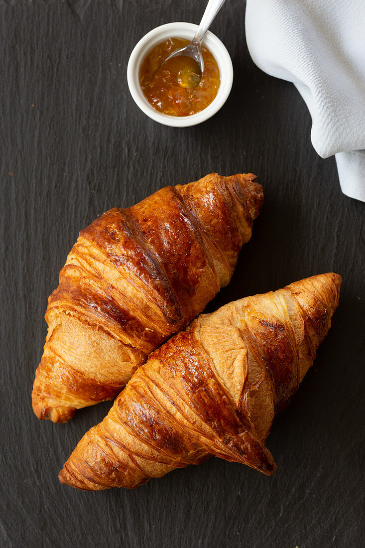 Two classic French flaky croissants with orange confiture