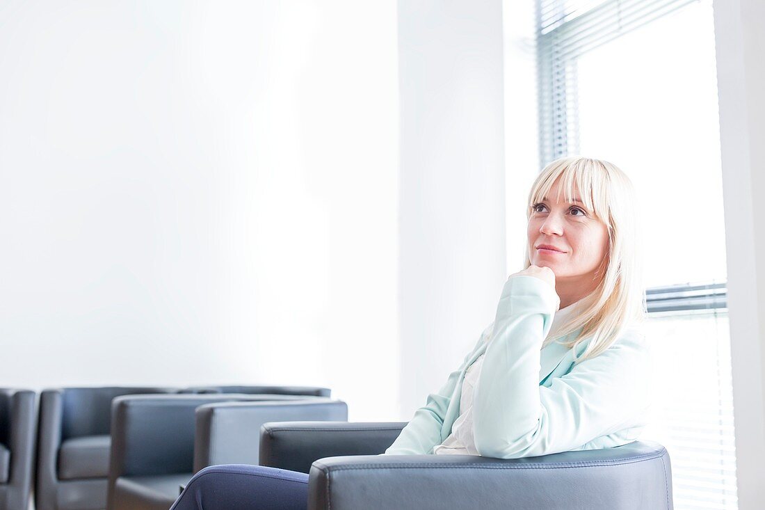 Pensive mid adult woman sitting in doctor's waiting room wit