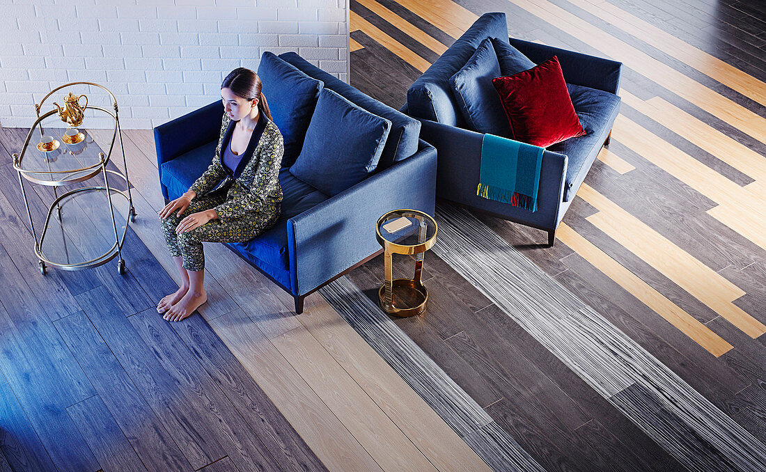 Living room with wooden floor in various shades, woman sitting on a blue two-seater, next to it a serving trolley and side table