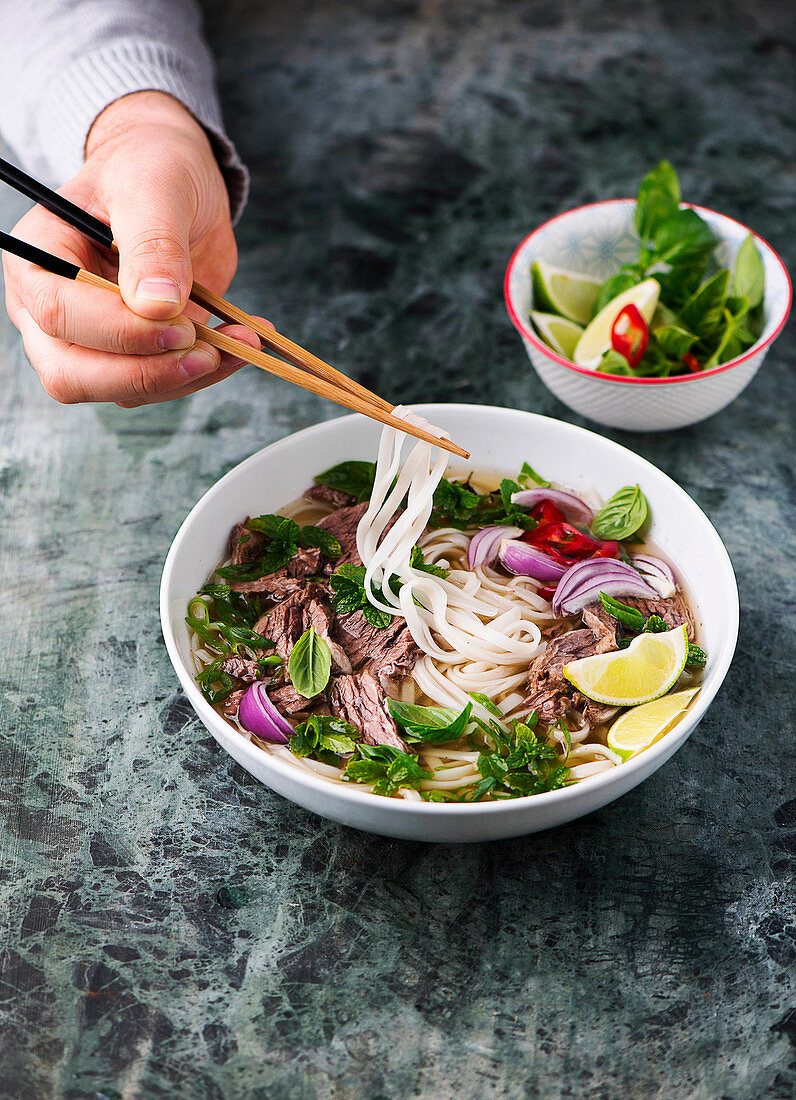 Person eats Pho Bo (soup with beef and rice noodles, Vietnam)