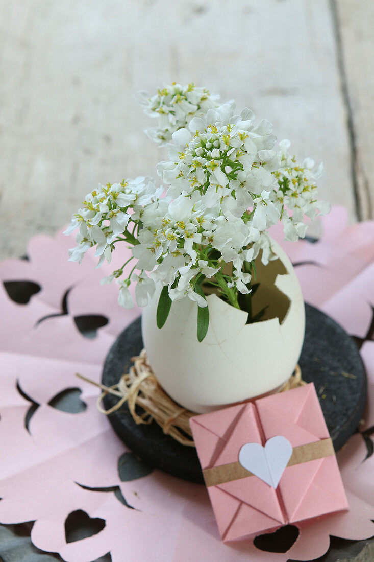 Easter arrangement of duck egg used as vase for small white flowers and origami envelope
