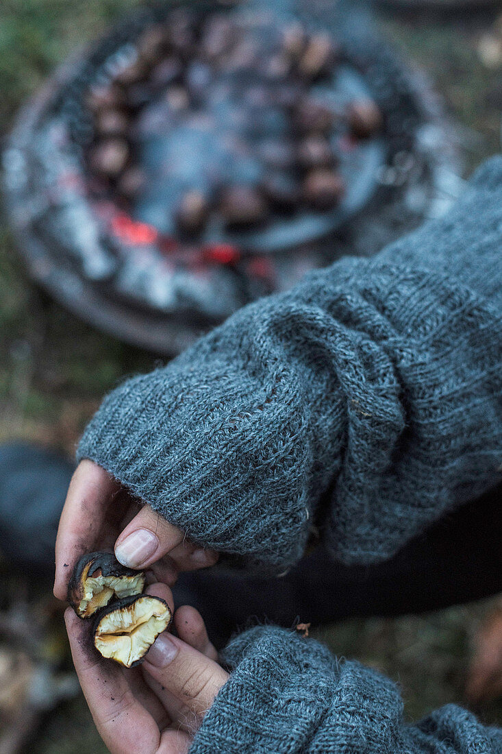 A woman breaking apart a roasted chestnut