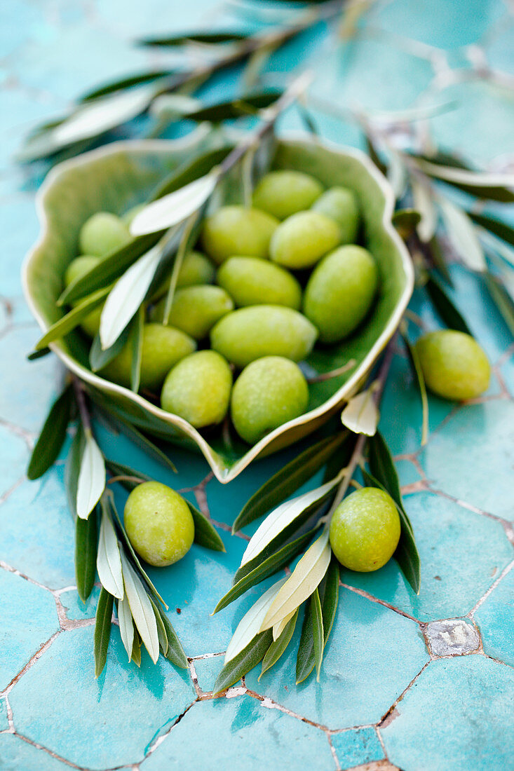 Grüne Oliven in Schälchen und Olivenzweige