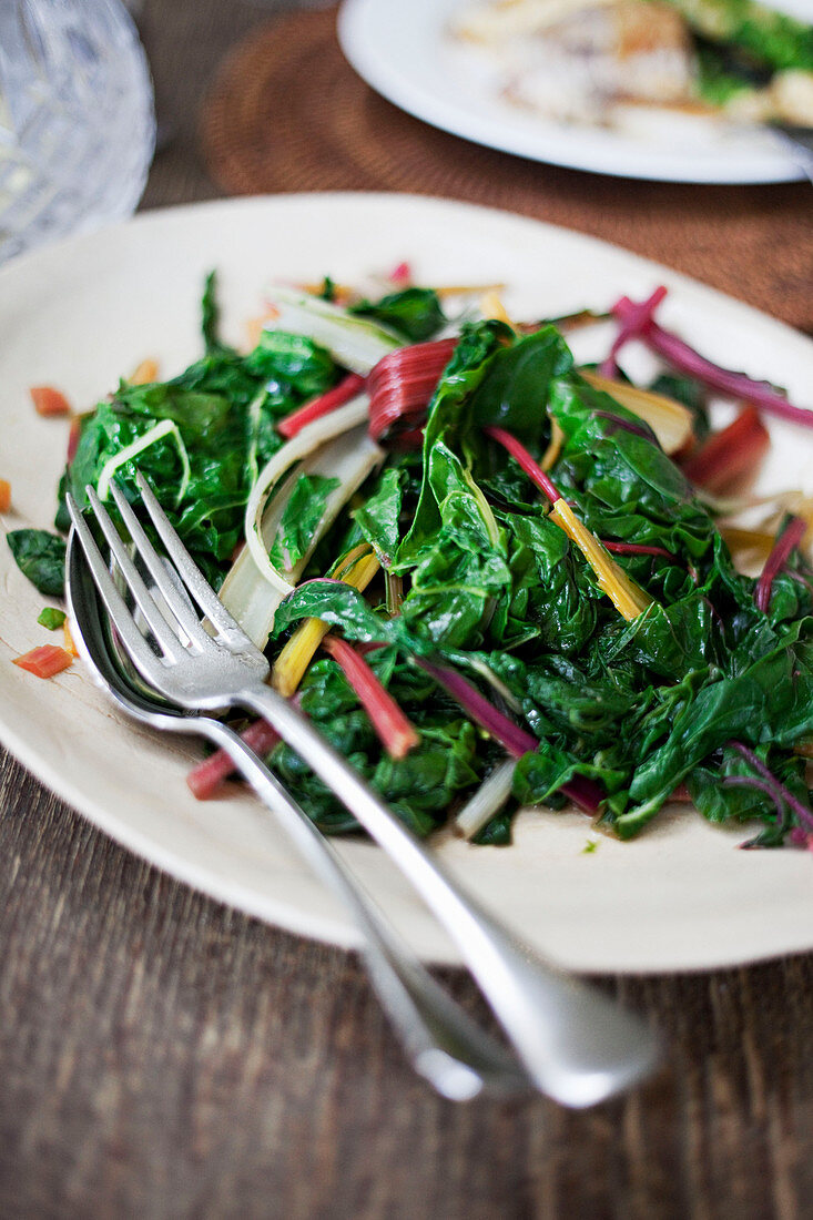 Rainbow chard steamed and presented on a platter with knife and fork