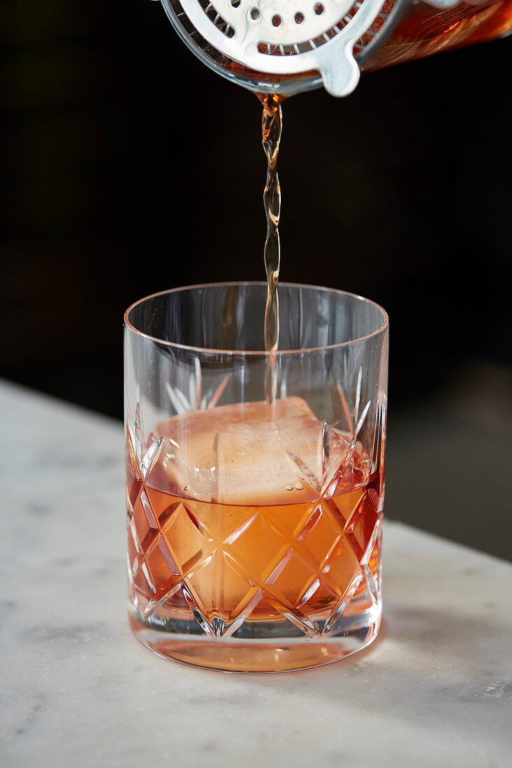 Old Fashioned Cocktail durch Barsieb in Glas gießen