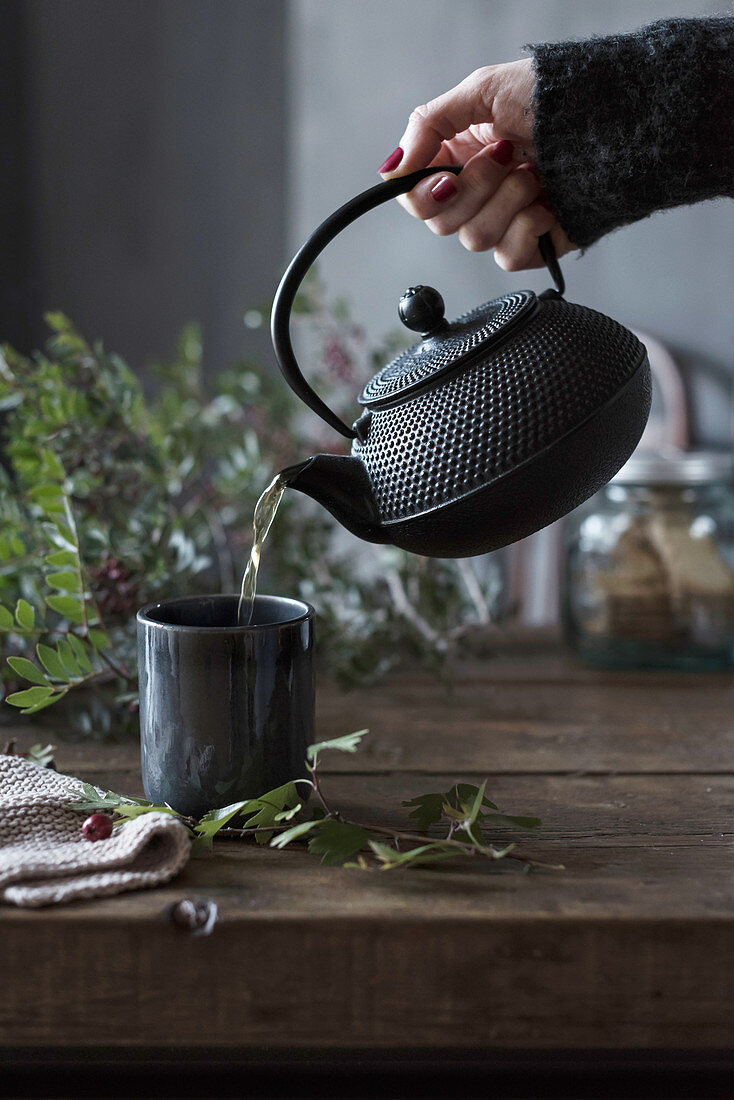 Hand of unrecognizable person pouring tea from pot to cup on a table