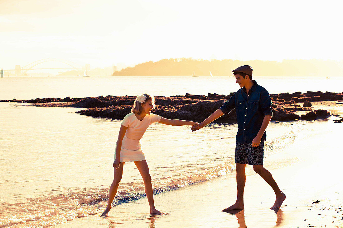 Junges Paar hält Händchen am Strand im Sonnenuntergang