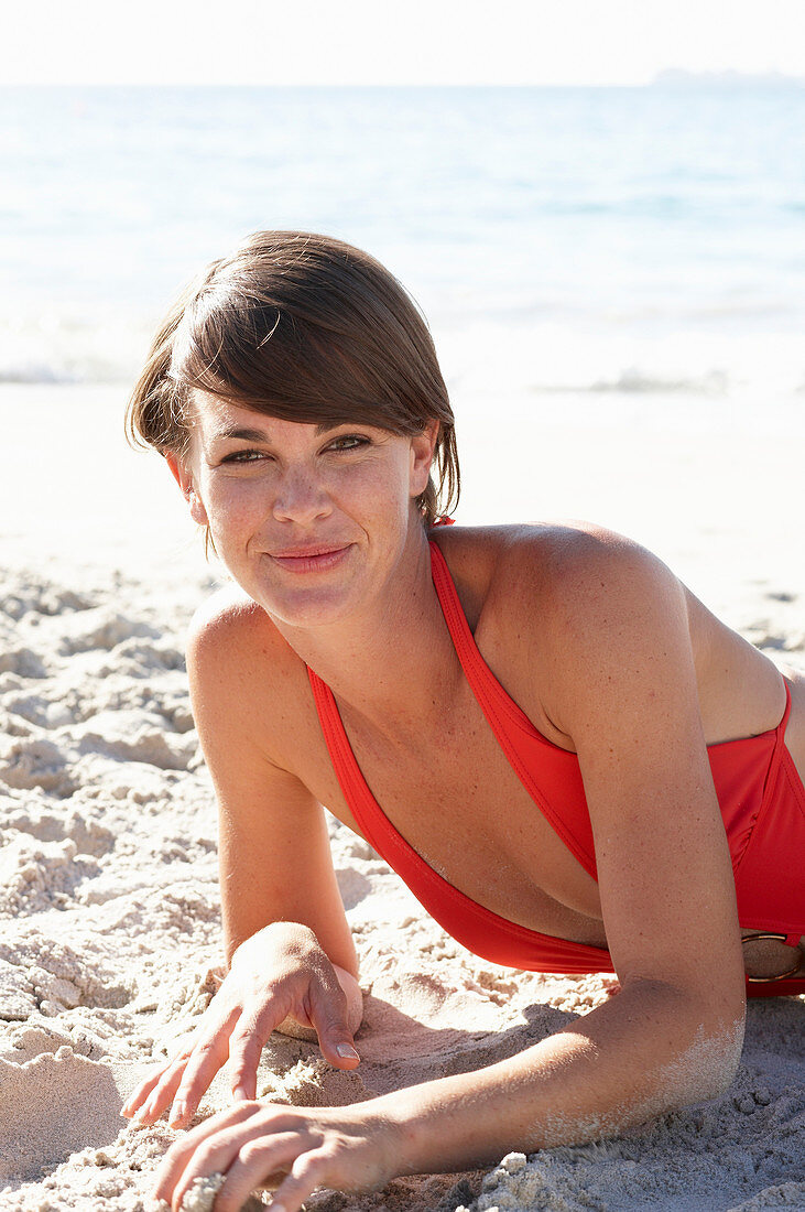 Reife brünette Frau in rotem Badeanzug am Strand