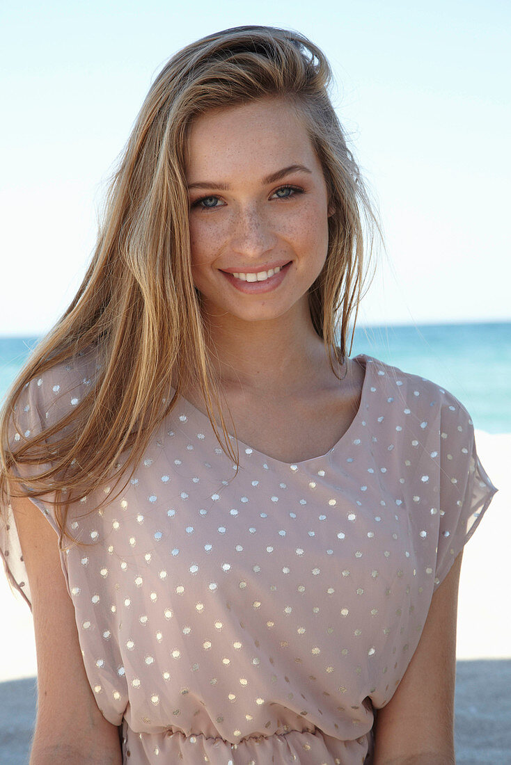 A young blonde woman on a beach wearing a beige polka-dot dress