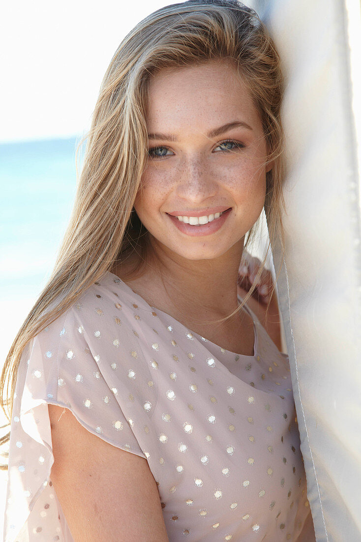 A young blonde woman on a beach wearing a beige polka-dot dress