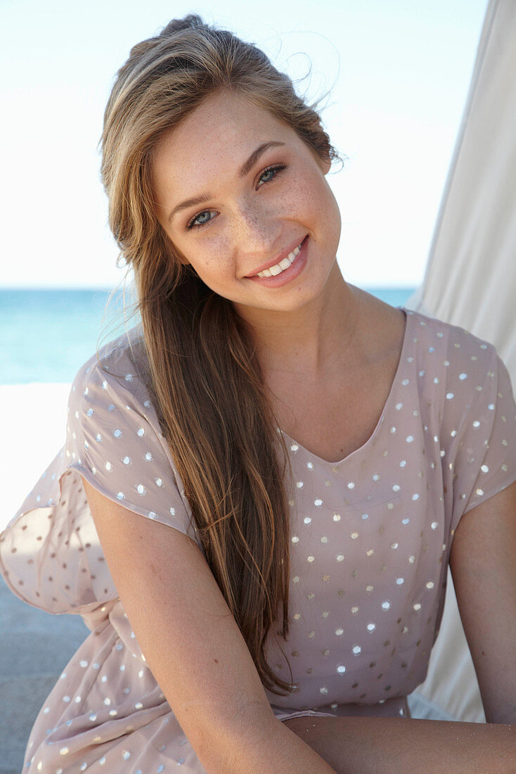 A young blonde woman on a beach wearing a beige polka-dot dress