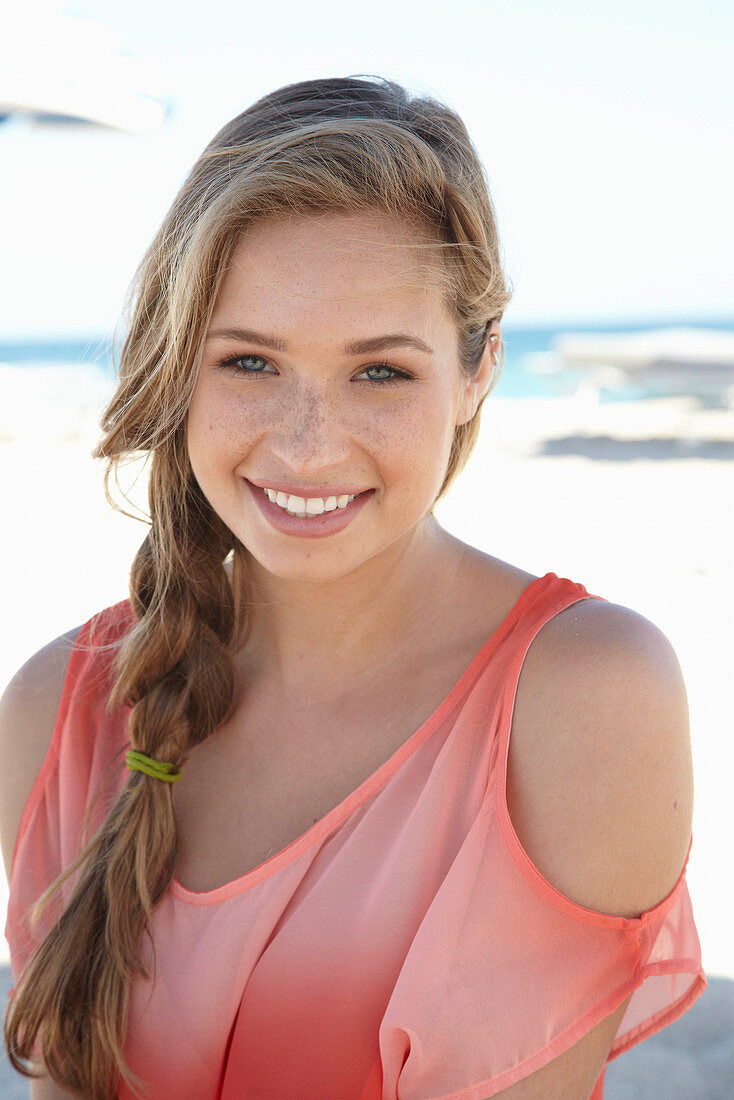 Junge blonde Frau in lachsfarbenem schulterfreiem Top am Strand