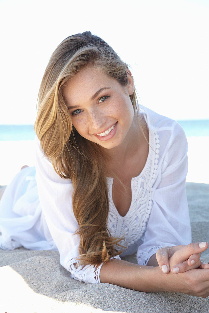 A young blonde woman on a beach wearing a white summer dress