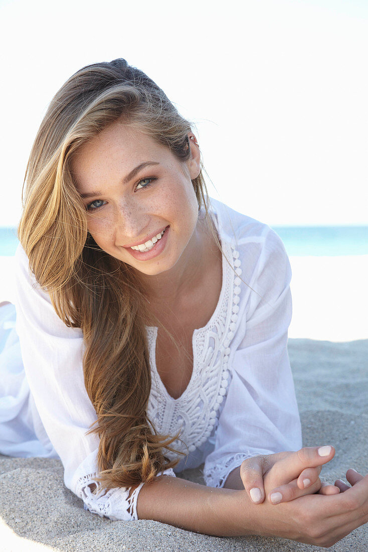 A young blonde woman on a beach wearing a white summer dress