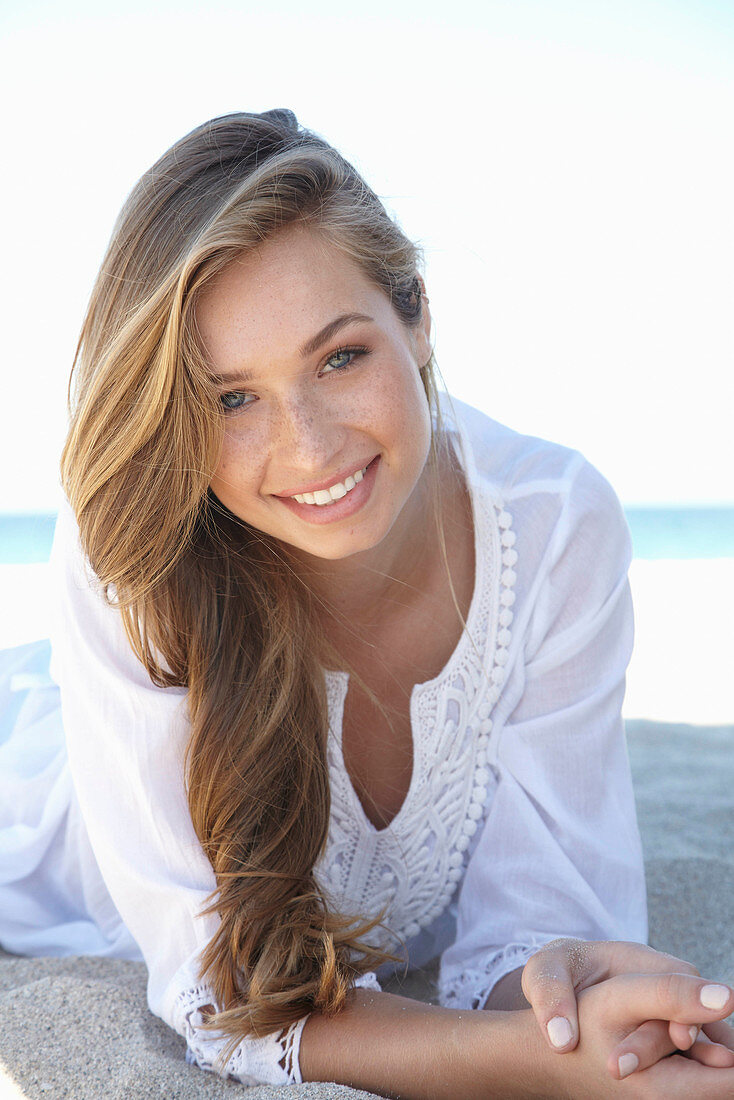 A young blonde woman on a beach wearing a white summer dress