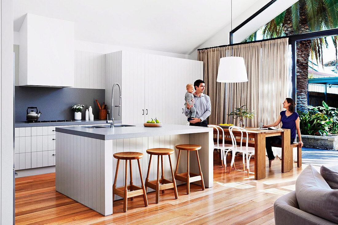 Open kitchen with kitchen island and dining area in front of patio door, family with small child at the dining table