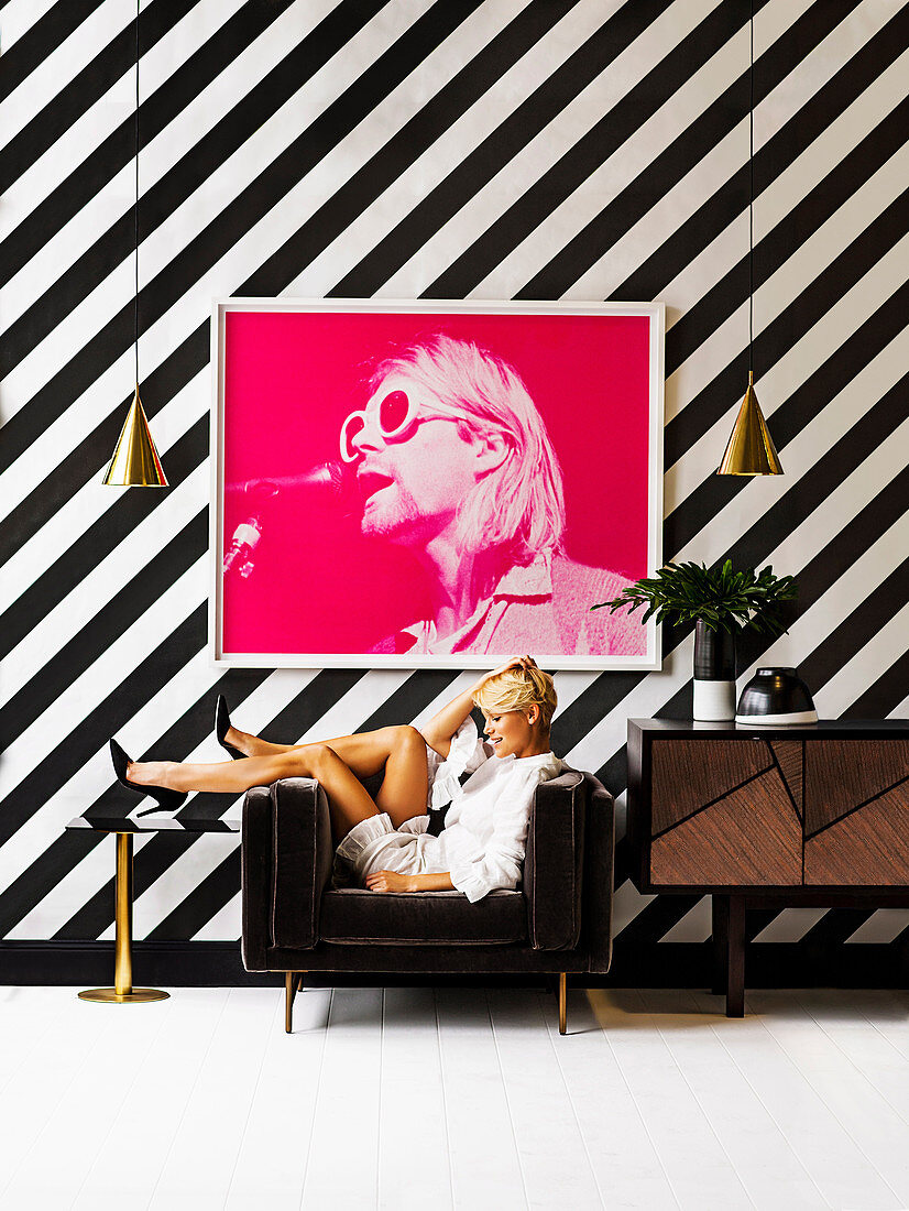 Photography in pink on a black and white striped wall, blonde woman in a brown armchair